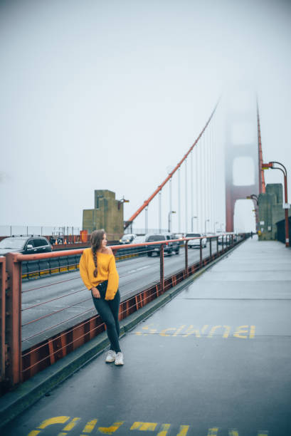 donna in maglione giallo cammina lungo ponte - bay bridge car traffic transportation foto e immagini stock