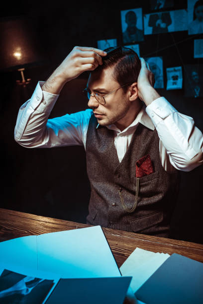 istock Pensive detective combing hair with comb in dark office 1150780221