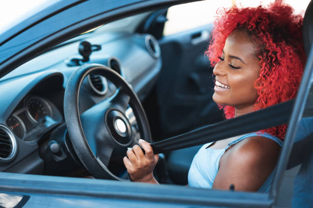 donna sorridente che si mette la cintura di sicurezza - car insurance women driving foto e immagini stock