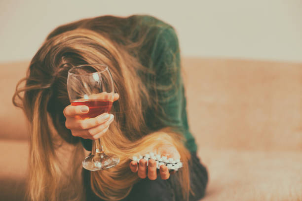 Depressed woman drinking alcohol and pills stock photo