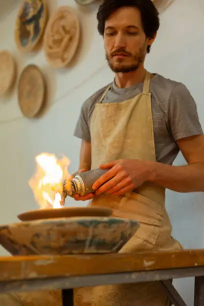 Process of creating. Calm serious man carrying gas-burner while baking fresh plate as last step in manufacturing