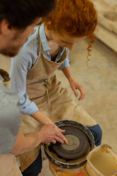 istock Curious ginger girl sitting on a chair and learning pottery wheel technique 1150786328