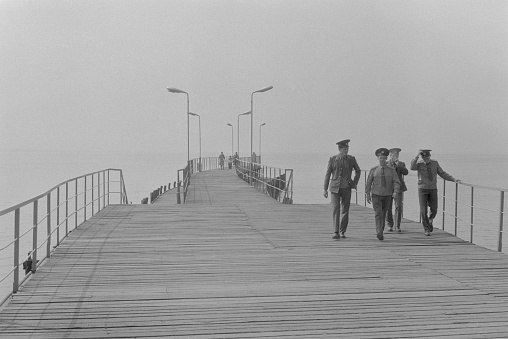 Sukhumi, Abkhazia, USSR - July 14, 1988: Four soldiers of soviet army walk on wooden pier on the shore of Black Sea