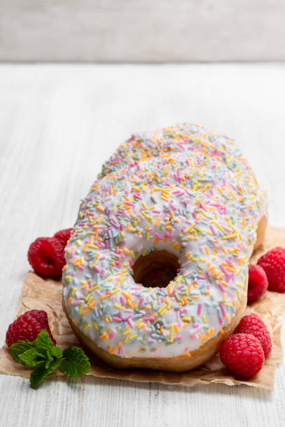 istock Pink doughnuts with sprinkles and fresh raspberry on white wooden table 1150787794