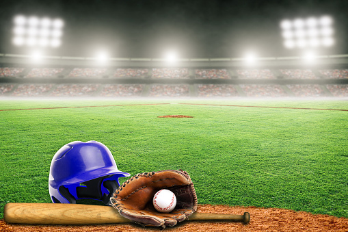 Blue baseball helmet, bat, glove and ball on field at brightly lit outdoor stadium. Focus on foreground and shallow depth of field on background and copy space. Fictitious stadium created in Photoshop.