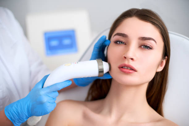 Beautician doctor doing rf-lifting procedure for flawless woman face laying on medical chair in a beauty salon. Hardware cosmetology. Patient receiving electric facial massage. Skin rejuvenation and wrinkle smoothing. médico esteticista haciendo el procedimiento de rf-levantamiento para la cara perfecta mujer acostado en un salón de belleza. cosmetología de hardware. paciente recibiendo masaje facial eléctrico. rejuvenecimiento de la piel y suavizado de arrugas