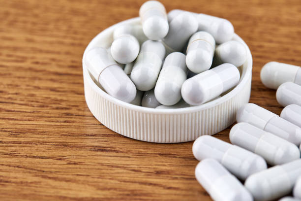 istock Many white capsules in plastic cap on wooden background 1150829161