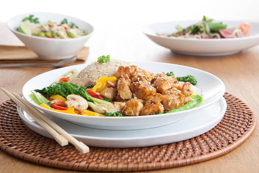 a bowl of chicken stir fry with rice and chopsticks