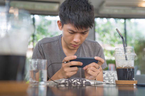 młody biznes azjatyckich mężczyzn za pomocą inteligentnego telefonu gry mobilnej i zrelaksować się z zakupów online w jego powołań - wireless technology serious education enjoyment zdjęcia i obrazy z banku zdjęć