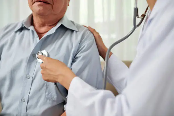 Close-up of female doctor in white coat listening to breathe of senior man during his visit at hospital