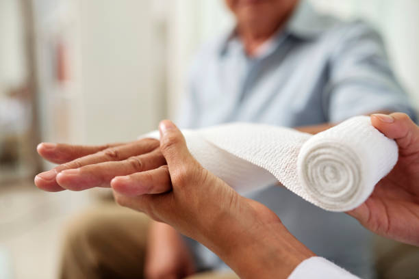 Doctor putting bandage on patient's hand Close-up of nurse holding and bandaging hand of senior patient at hospital wound stock pictures, royalty-free photos & images