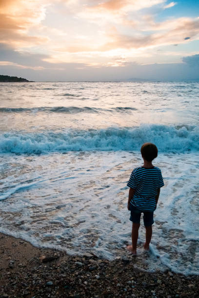 istock Little boy standing on the beach in water foam 1150877597