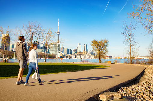 Two friends walking in Toronto Trillium park with city skyline in the background, photographed in late afternoon on a sunny Springtime day.