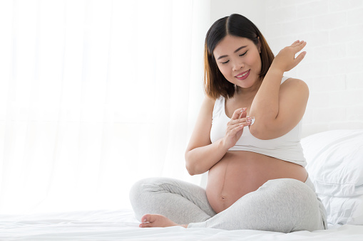 Pregnant woman takes care of elbow using cosmetic cream, Asian model