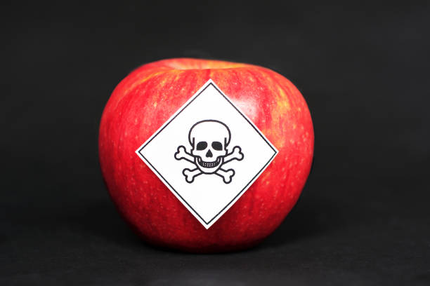 conceito de resíduos do insecticida em produtos alimentares agrícolas perigosos aos seres humanos, mostrando uma maçã vermelha com a etiqueta do símbolo do veneno no fundo preto - intoxicação de substâncias - fotografias e filmes do acervo