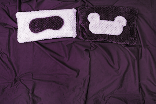 Two Pillow and Two Eye mask for sleeping from fur on bed with purple cotton sheet. Top  view. Flat lay.
