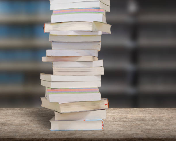 istock Stacking books on wood desk with blur bookshelfs background. 1150883759
