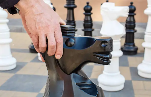 man moving giant chess piece horse outdoor on the city street. hands closeup