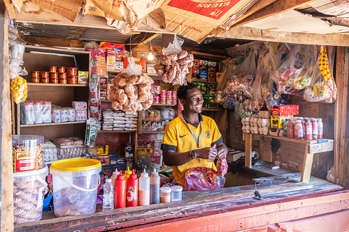 Supermarket kiosk and african attendant smiling in Alexandra Township, Johannesburg. Alexandra also known as Alex was developed since 1912 and allocated for the africans in the apartheid era, it is now home to over 400 000 inhabitants in an area 7,6 km2, and forms part of Johannesburg city council.