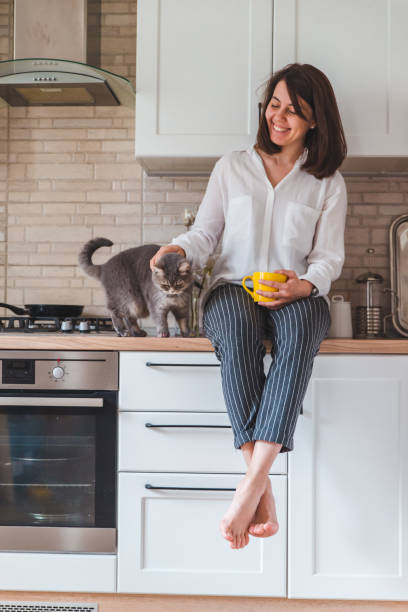 istock woman sitting on kitchen table with cat drinking tea from yellow mug 1150892253