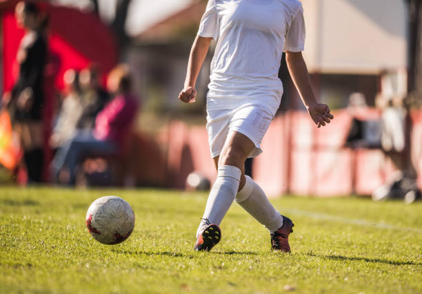 A young Caucasian soccer girl is practicing dribbling skills and balance with a ball in the soccer field.