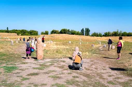 Tokmok, Kyrgyzstan - Avgust 23, 2017: Tourists at historic grave stone markers with faces, from 6th century, gathered in the field,  near  Burana Tower in Kyrgyzstan.