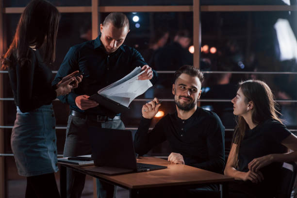 istock Holding notepad with documents. Team of young business people works on their project at night time in the office 1150898235