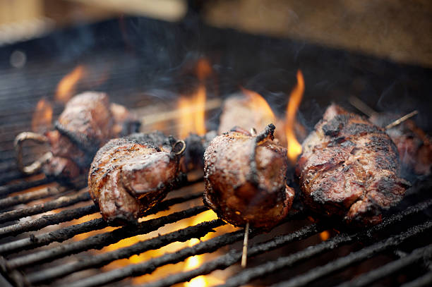 venison steaks wrapped in bacon on gas bbq grill with flames and smoke
