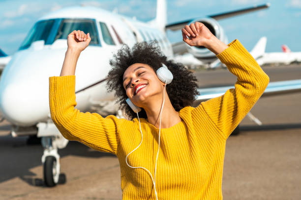 jeune fille heureusement appréciant la musique au-dessus du casque en face d’un jet privé stationné sur un tarmac d’aéroport - status symbol audio photos et images de collection