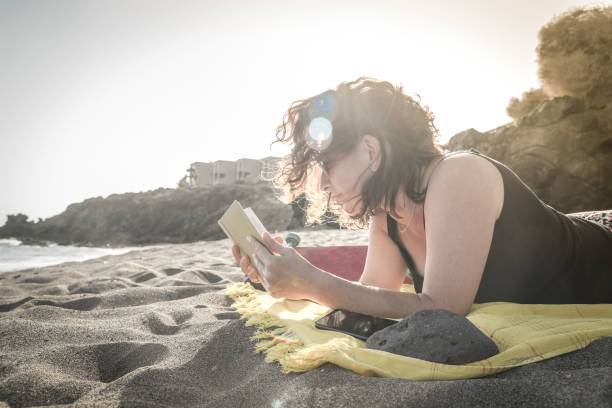 istock Woman Reading Book While Relaxing At Beach 1150905527