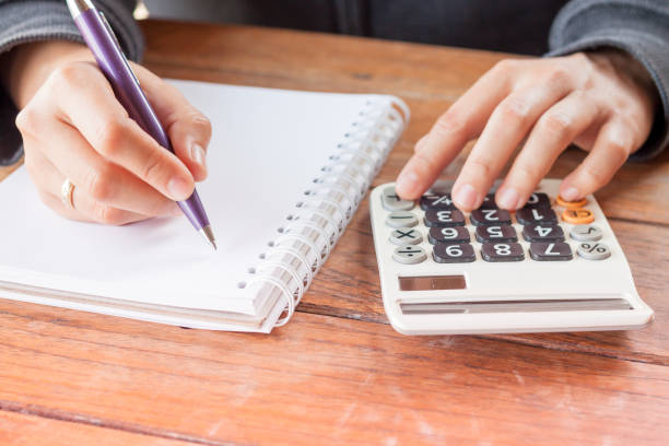 istock Close-Up Of Hand Writing In Book While Using Calculator On Table 1150906964