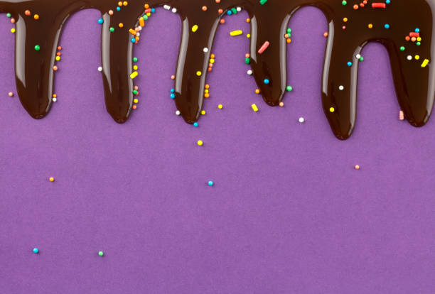 istock Cake topping colour sprinkles with chocolate flowing down on violet background - space for text 1150908723