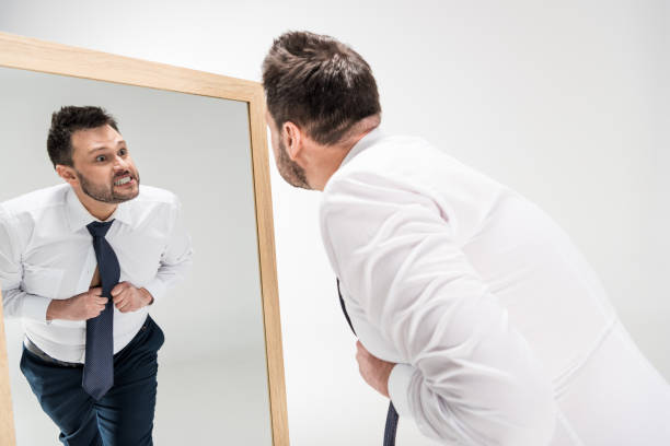 istock angry overweight man in formal wear looking at reflection in mirror on white 1150909939