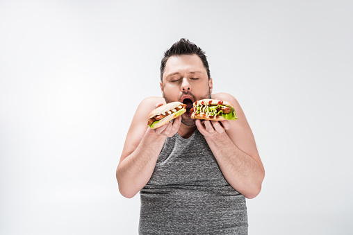overweight man eating hot dogs isolated on white