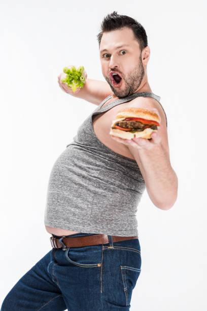 istock excited overweight man looking at camera while holding celery and burger isolated on white 1150910234