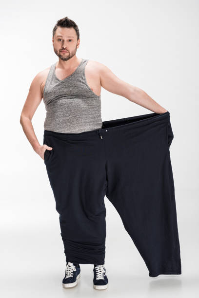 istock overweight man holding oversize pants after weight loss and looking at camera on white 1150910347