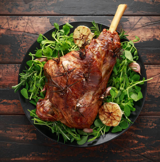 ラム肉のローストとローズマリーとニンニクの足。ブラックプレート上, 木製テーブル - savoury slice ストックフォトと画像