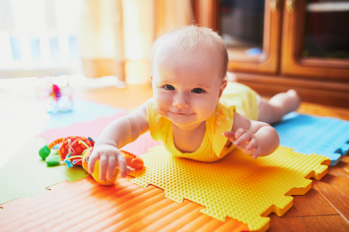 Happy smiling baby girl lying on colorful play mat on the floor