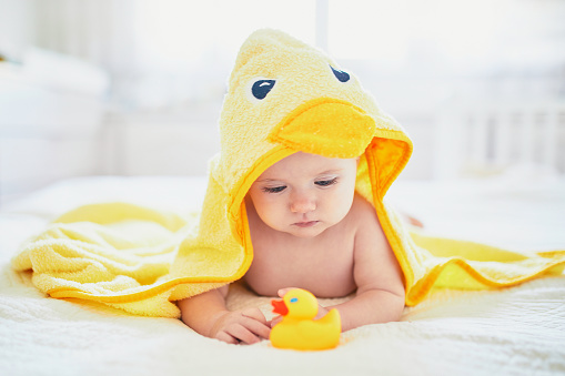 Cute little girl playing with rubber duck after having bath. Happy kid in yellow towel