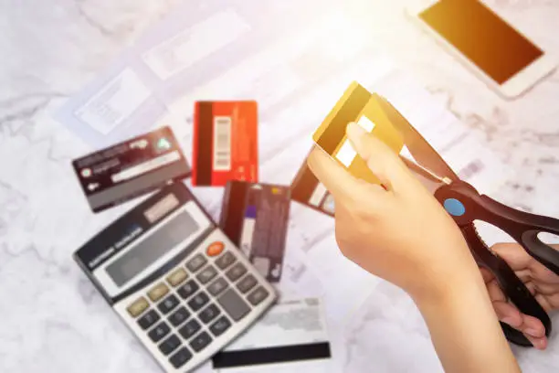 Photo of women use scissors to cut credit cards in hand with many credit card and statement on table for background