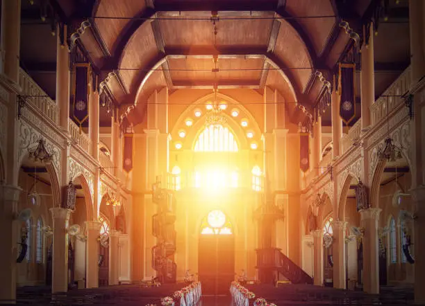 Photo of interior view of empty church with wooden bench decorated with flower bouquet, sunlight through church stained glass window