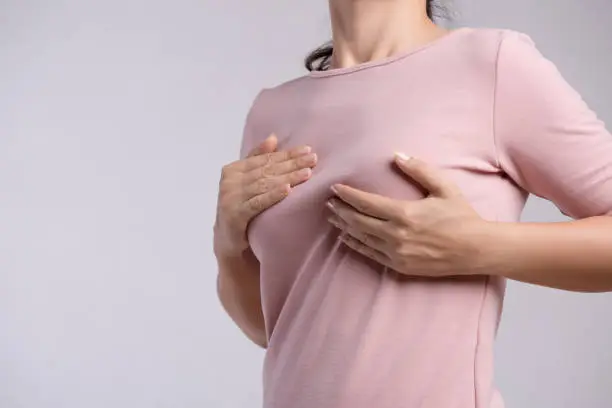 Photo of Woman hand checking lumps on her breast for signs of breast cancer on gray background. Healthcare concept.