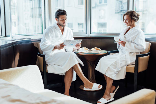 istock cheerful woman looking at handsome man reading newspaper in bathrobe 1150936082