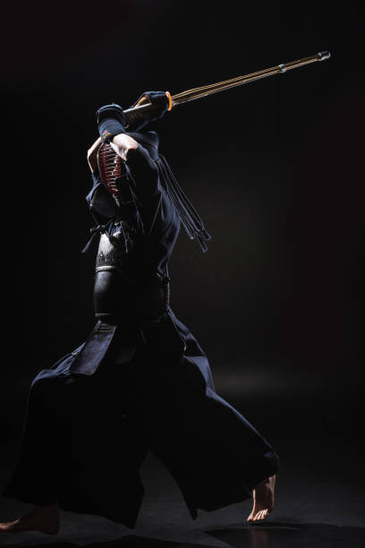 Full length view of kendo fighter in armor practicing with bamboo sword on black Full length view of kendo fighter in armor practicing with bamboo sword on black kendo stock pictures, royalty-free photos & images