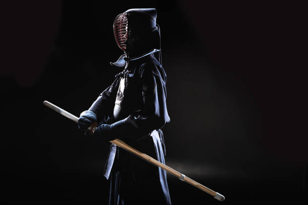 Side view of kendo fighter in traditional helmet holding bamboo sword on black Side view of kendo fighter in traditional helmet holding bamboo sword on black kendo stock pictures, royalty-free photos & images