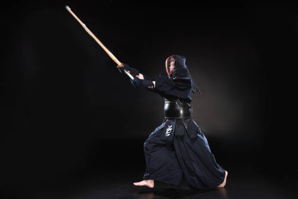 istock Full length view of kendo fighter in armor practicing with bamboo sword on black 1150937128