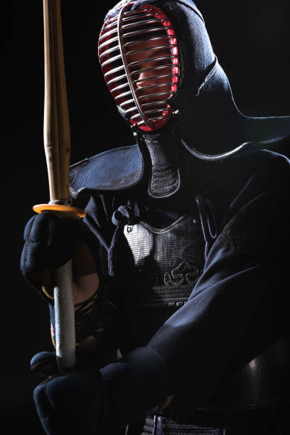 istock Kendo fighter in helmet holding bamboo sword isolated on black 1150937172