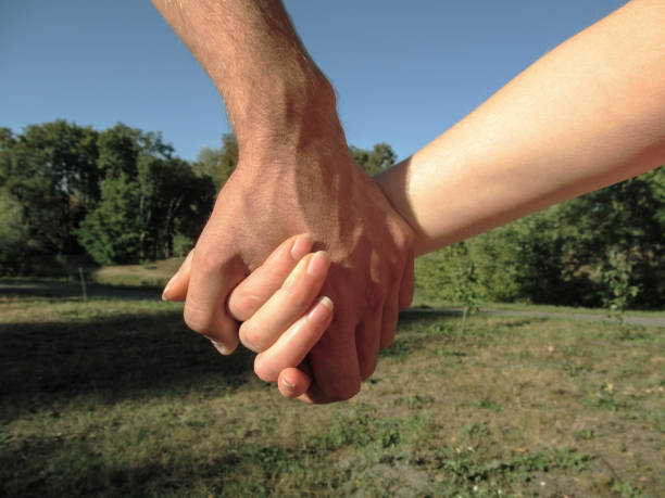 männliche hand hält weibliche hand auf dem hintergrund der sommer-herbst-landschaft im park, nahaufnahme - two parent family naked men couple stock-fotos und bilder