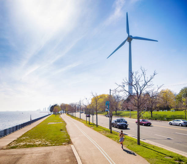 Woman running in Toronto next to Lakeshore boulevard and a wind turbine Elevated view of woman running in Toronto next to Lakeshore boulevard and a wind turbine on a sunny Springtime day. Cars are rolling by on the road. sustainable energy toronto stock pictures, royalty-free photos & images