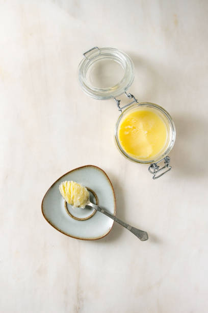 Melted ghee butter Homemade Melted ghee clarified butter in open glass jar and spoon on saucer over white marble background. Flat lay, space clarified butter stock pictures, royalty-free photos & images